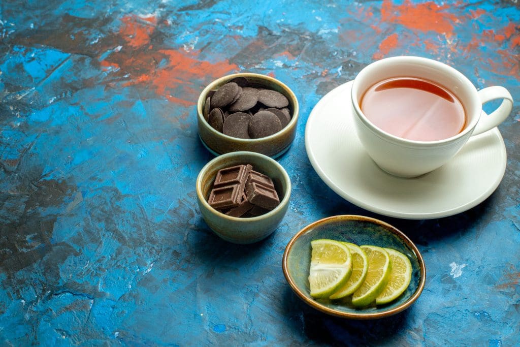 bottom view cup tea chocolates lemon slices blue red surface free space LIV Hospital