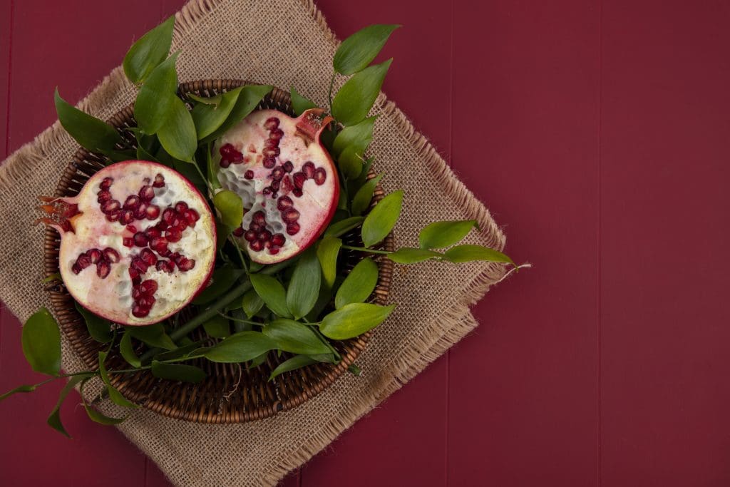 top view half cut pomegranate with leaves basket sackcloth red surface LIV Hospital