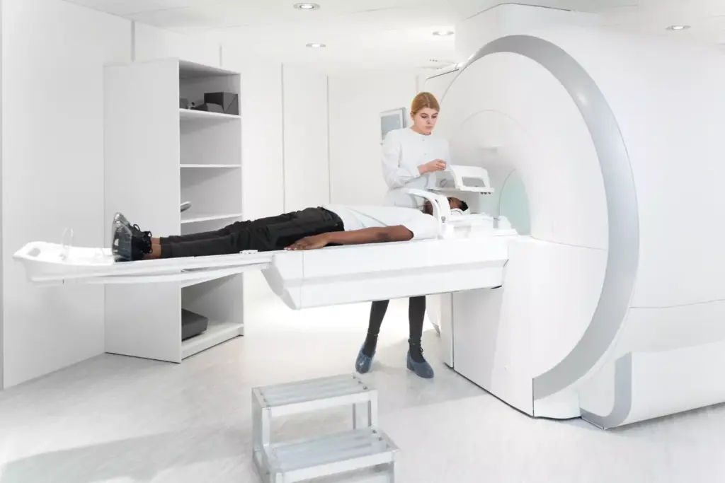 A clinical imaging examination room with bright, natural lighting streaming through large windows. In the foreground, a high-resolution MRI scan of a human knee joint is displayed on a large, high-definition medical monitor. The scan clearly shows the torn, irregular structure of the anterior cruciate ligament (ACL). In the middle ground, a medical professional, wearing a white lab coat, examines the MRI scan intently, assessing the extent of the injury. The background features various medical equipment and diagnostic devices, conveying a sense of a professional, clinical environment focused on accurate ACL diagnosis and treatment planning.