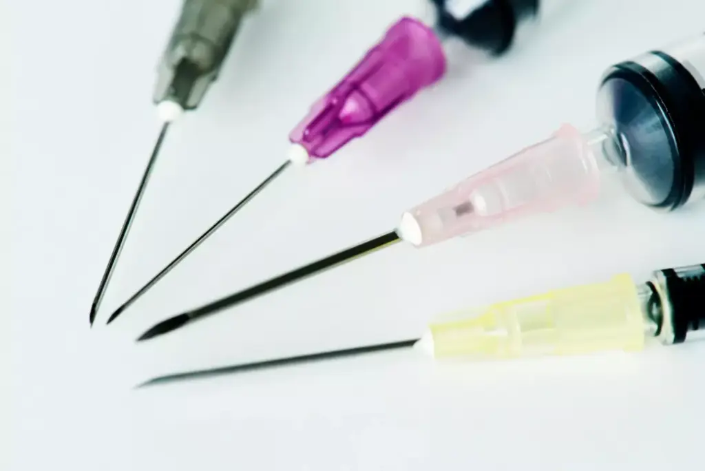 A close-up view of a selection of oncology needles, precisely arranged on a sterile medical tray. The needles are of various sizes and gauges, gleaming under bright, directional lighting that casts dramatic shadows, highlighting their sharp, precise forms. The background is blurred, creating a sense of clinical focus on the instruments. The image conveys a sense of medical expertise and the importance of carefully selecting the appropriate needle for specific cancer treatment procedures, such as chemotherapy administration or bone biopsy for metastasis diagnosis. A close-up view of a selection of oncology needles, precisely arranged on a sterile medical tray. The needles are of various sizes and gauges, gleaming under bright, directional lighting that casts dramatic shadows, highlighting their sharp, precise forms. The background is blurred, creating a sense of clinical focus on the instruments. The image conveys a sense of medical expertise and the importance of carefully selecting the appropriate needle for specific cancer treatment procedures, such as chemotherapy administration or bone biopsy for metastasis diagnosis.