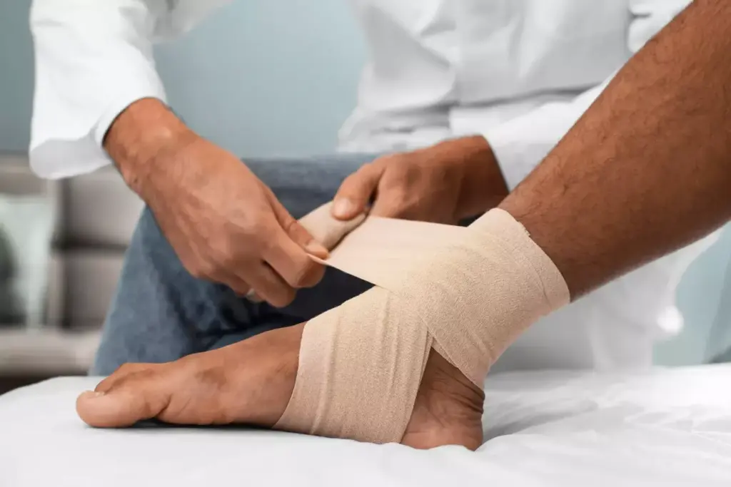 A crisp, well-lit medical examination room. In the foreground, a close-up view of a human ankle, swollen and discolored, with compression bandages applied. In the middle ground, the hands of a healthcare professional gently palpating the ankle, assessing the extent of the injury. The background features medical equipment, shelves of supplies, and a neutral-toned color scheme, conveying a clinical, professional atmosphere. Bright, natural lighting from large windows casts an even illumination across the scene, highlighting the details of the treatment process. The overall mood is one of focused, attentive care, reflecting the specialized knowledge required to properly diagnose and treat an ankle sprain.