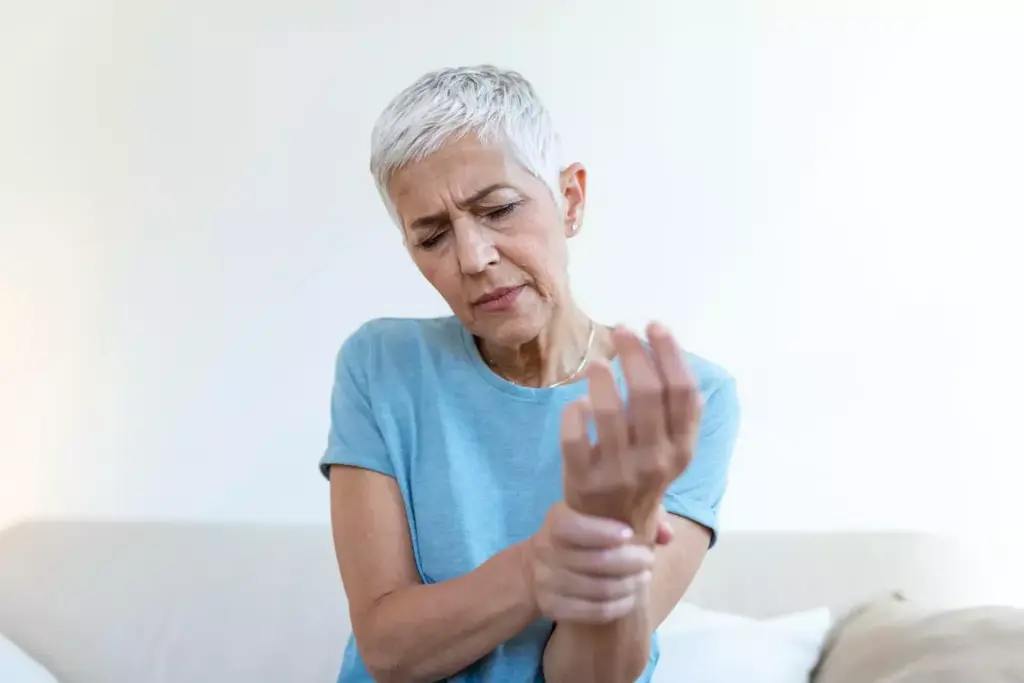 A person experiencing debilitating arthritis pain, gripping their aching hand in a dimly lit room. The foreground features the close-up of the afflicted hand, with prominent, swollen knuckles and wrinkled skin. The middle ground showcases the person's pained expression, their face partially obscured in shadow, conveying a sense of discomfort and frustration. The background is hazy, with a soft, warm glow emanating from a nearby lamp, creating a pensive, introspective atmosphere. The lighting is subdued, casting dramatic shadows that emphasize the severity of the condition, while the lens is focused on the hand, drawing the viewer's attention to the source of the pain.