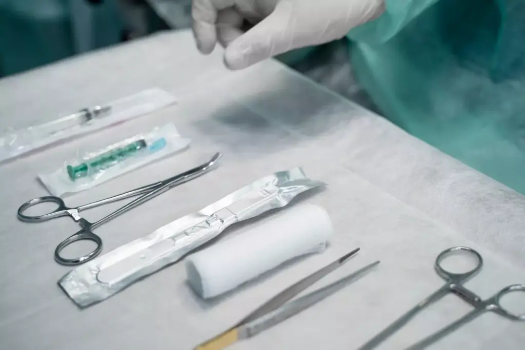 A well-lit, high-angle view of a surgical table, meticulously prepared for an ACL reconstruction procedure. The table is covered in sterile blue drapes, with medical instruments and supplies neatly arranged. In the foreground, a pair of gloved hands holds a scalpel, ready to make the initial incision. The background features the blurred silhouettes of medical professionals, creating a sense of anticipation and professionalism. The overall atmosphere conveys a clinical, yet reassuring environment, as the stage is set for the intricate surgery to come.