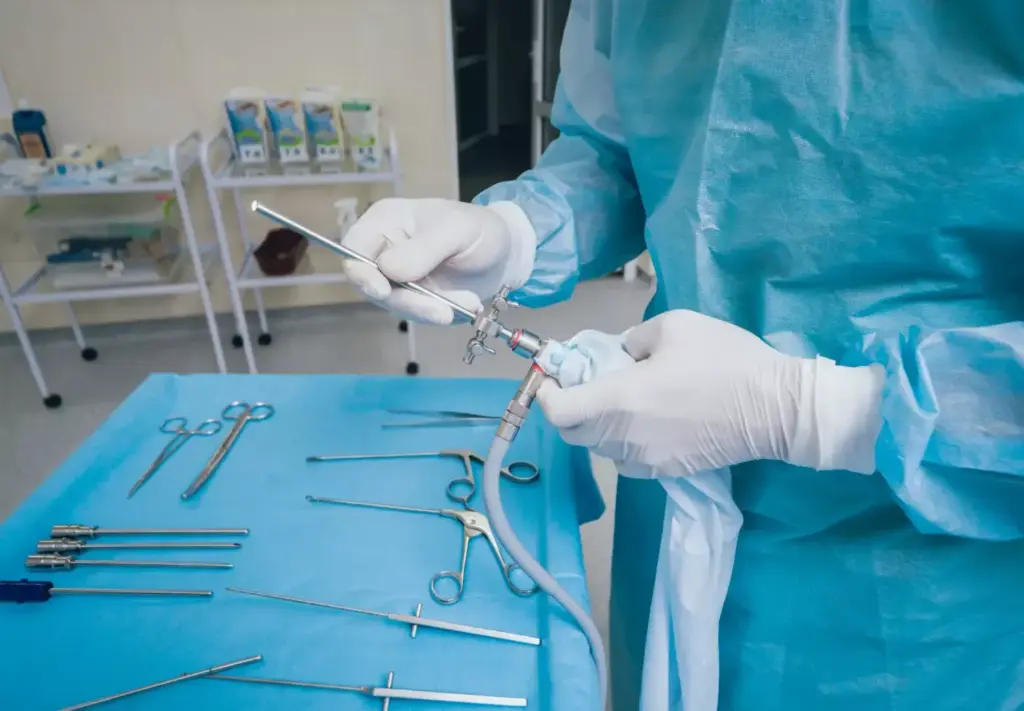 A well-lit, high-resolution image of a professional medical setup for laparoscopic surgery. In the foreground, a set of stainless steel laparoscopic instruments including graspers, scissors, and an energy device. In the middle ground, a modern laparoscopic camera and a light source. In the background, a large, high-definition display showing a detailed view of the surgical site. The scene conveys a sense of precision, technology, and the specialized nature of minimally invasive surgery.