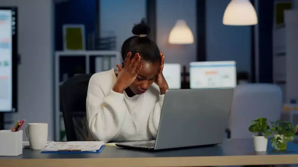 A woman sitting at a desk, her head in her hands, looking distressed. Behind her, a stack of medical bills and financial documents. The room is dimly lit, with a single lamp casting a warm glow. The atmosphere is one of worry and uncertainty, reflecting the financial burden of a breast cancer diagnosis and treatment. The image captures the emotional and financial toll on the patient, conveying the importance of financial assistance programs for breast cancer patients.