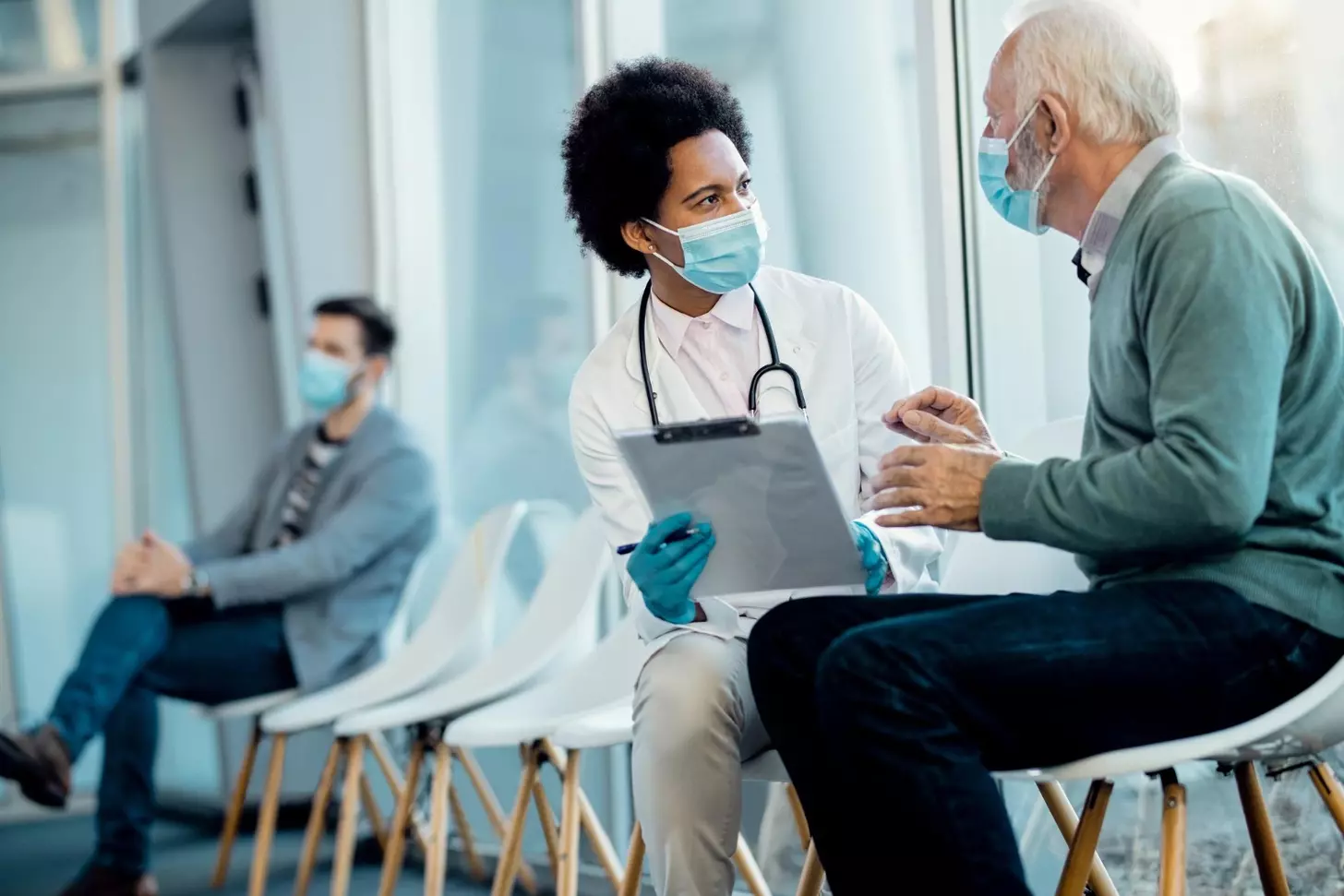 Black female doctor and senior man wearing face masks while talking