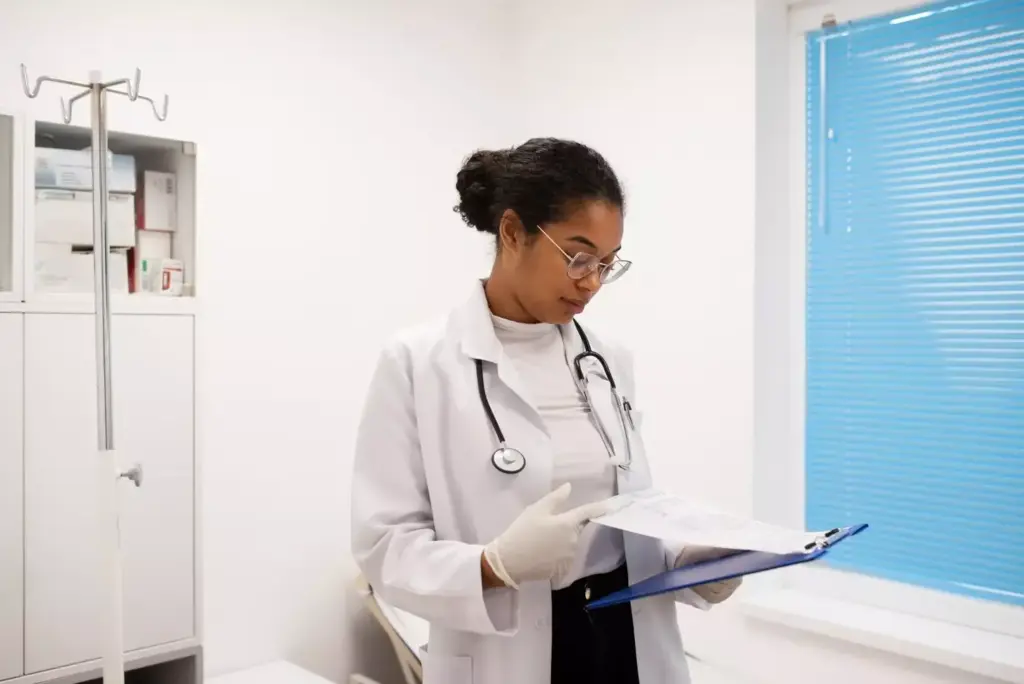 a portrait of an oncologist in a white lab coat, standing in a modern medical clinic with sleek minimalist decor and large windows letting in warm natural light. the oncologist is holding a clipboard and has a thoughtful, focused expression as they review patient information. the background is blurred, placing the oncologist in sharp focus. the image conveys a sense of professionalism, expertise, and a dedication to patient care.