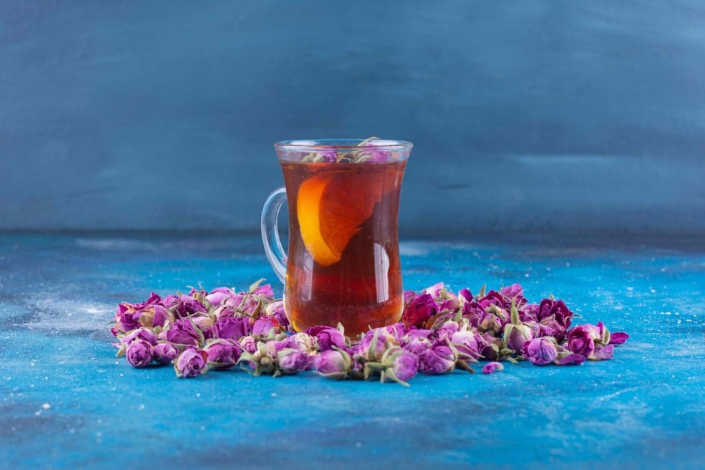 cup filled with fragrant herbal tea, set against a backdrop of vibrant green tea leaves and delicate purple flowers